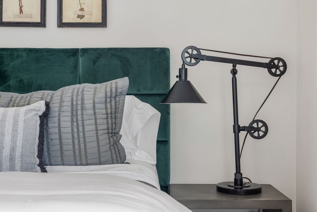 about-us-01 Elegant bedroom featuring a contemporary lamp, velvet headboard, and plush pillows.