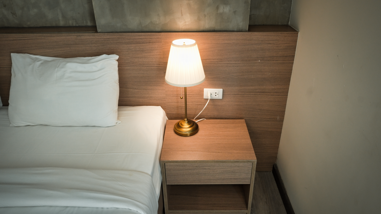 our-services-01 Elegant bedroom setup with a lamp on a wooden nightstand, creating a cozy ambiance.
