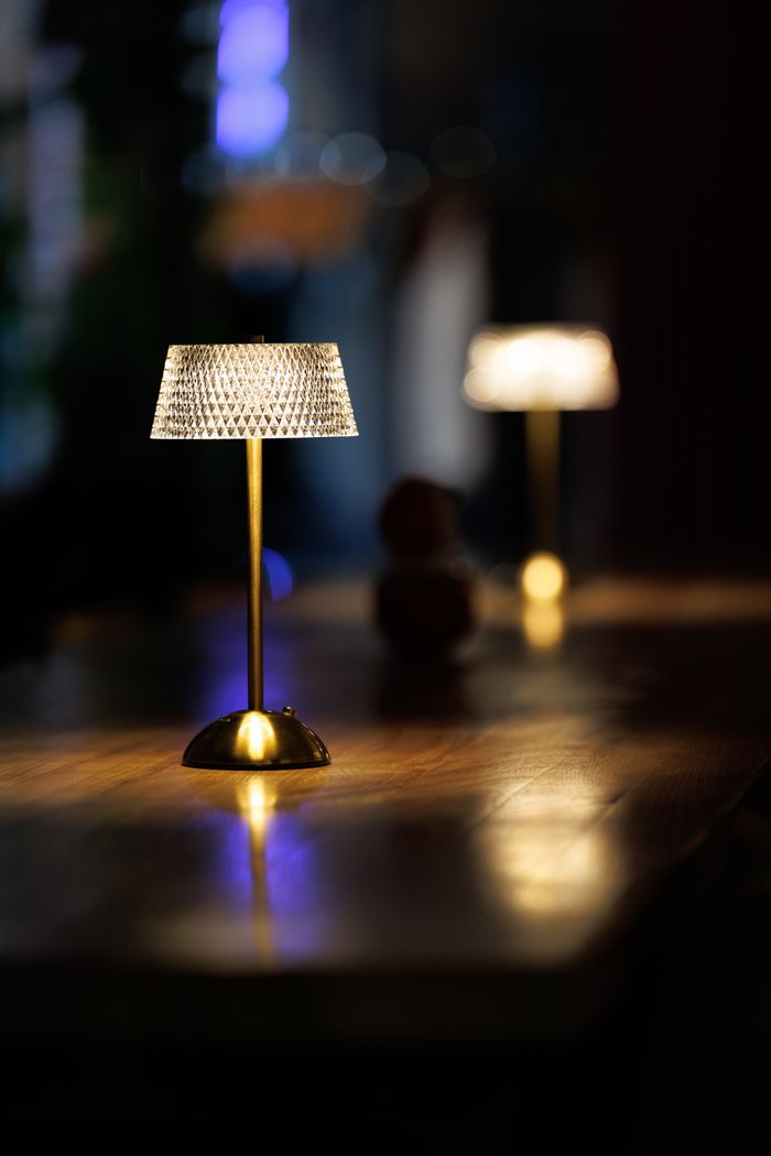our-services-03 A stylish table lamp with a crystal shade illuminates a wooden surface in a cozy indoor setting.
